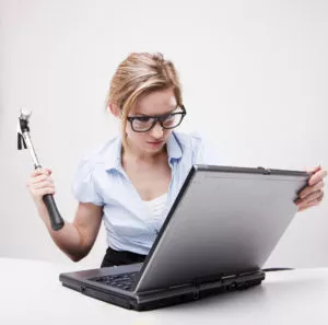 blond hair woman wearing business suit sitting in front of a computer with angry facial expression holding a hammer and wearing glasses