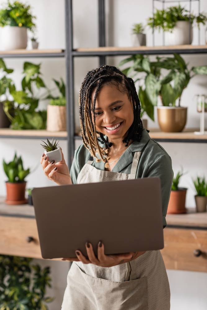 Woman in a plant shop holding a plant and her laptop