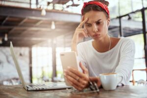 Upset woman entrepreneur looking at her phone next to her laptop